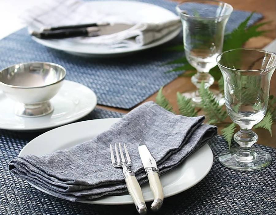 Elegant table setting with blue placemats, silverware, crystal glasses, and linen napkins from Cassandra’s Kitchen in Bluffton, SC – perfect for wedding gifts and entertaining.